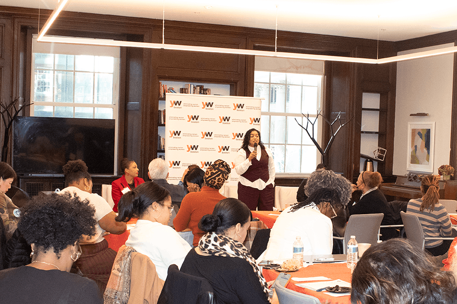 Senator Liz Miranda speaking in front of a crowd in the Kuumba Library with YW Boston signage behind her.