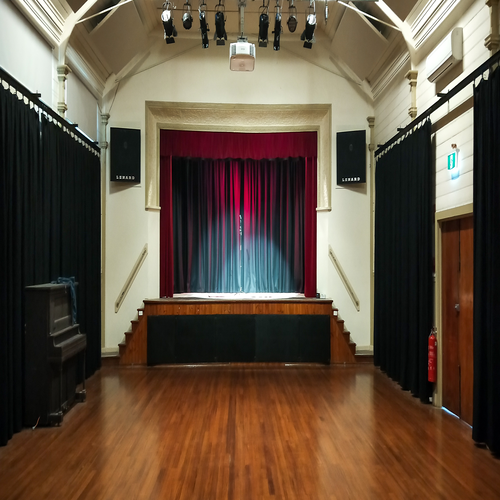 View of an empty hall with polished floorboards and a stage at the end framed by red curtains